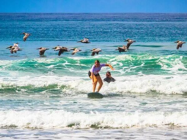 A beginner riding a small wave with her surf coach behind her at Kalon Surf